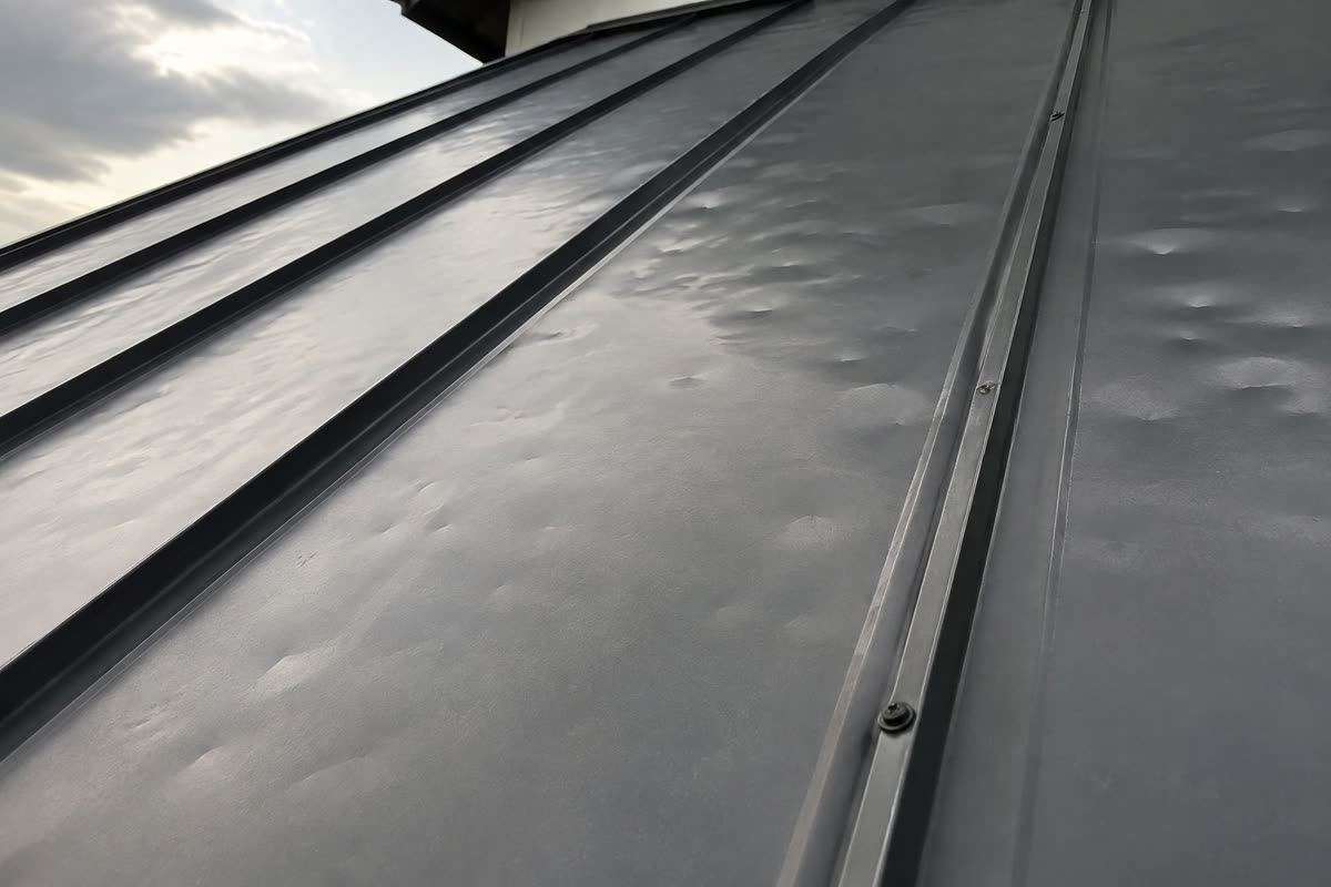 Illustration of scattered shallow hail dents on a charcoal standing seam metal roof